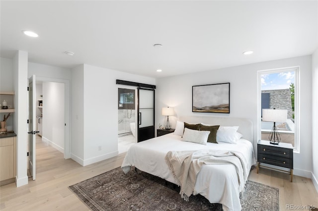 bedroom with light hardwood / wood-style flooring, a barn door, and ensuite bathroom