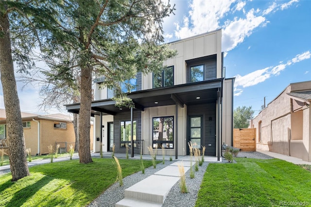 contemporary home with a porch, board and batten siding, a front yard, and fence