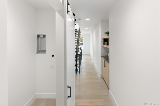 hallway featuring a barn door, baseboards, light wood-style flooring, and recessed lighting