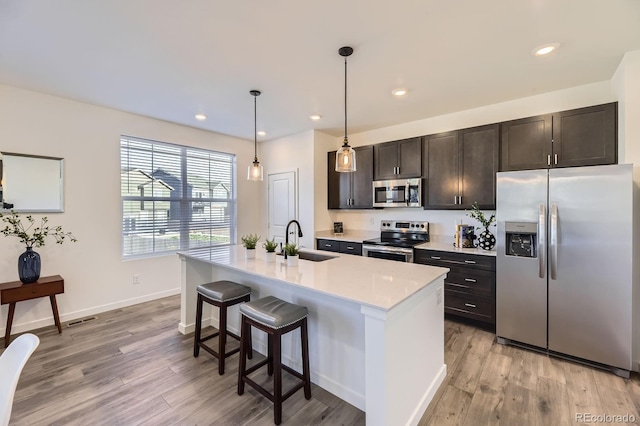 kitchen with a kitchen breakfast bar, appliances with stainless steel finishes, a sink, light countertops, and light wood-style floors
