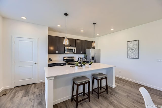 kitchen featuring a breakfast bar area, appliances with stainless steel finishes, a sink, and wood finished floors