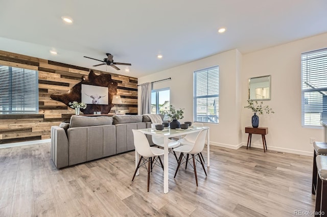 dining space featuring ceiling fan, wood walls, a wealth of natural light, and light wood-style flooring