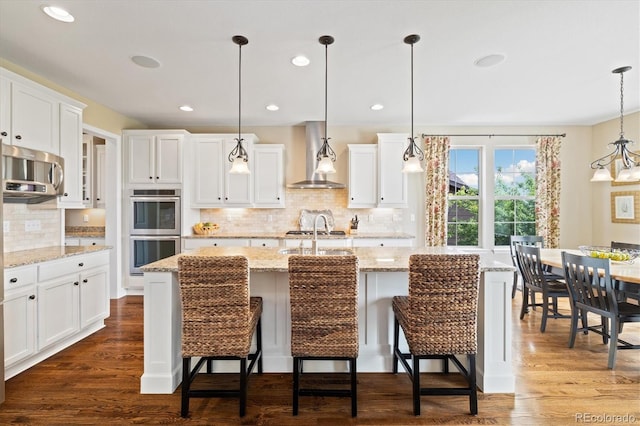 17452 W 83rd Pl, Arvada, CO 80007 - kitchen featuring wall chimney range hood, appliances with stainless steel finishes, white cabinetry, backsplash, and recessed lighting