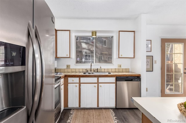 kitchen with a textured ceiling, stainless steel appliances, dark wood-style flooring, a sink, and white cabinetry