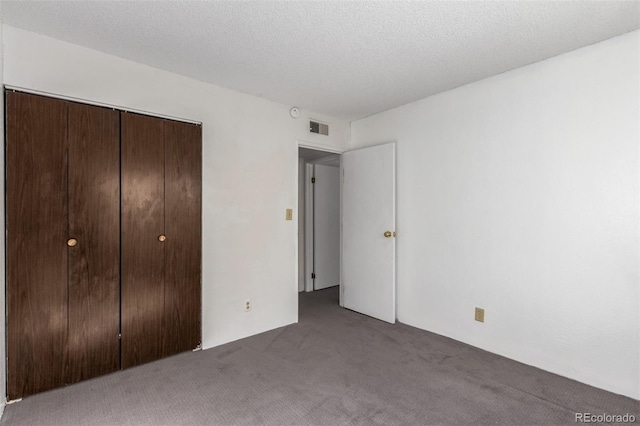 unfurnished bedroom featuring a textured ceiling, carpet floors, a closet, and visible vents