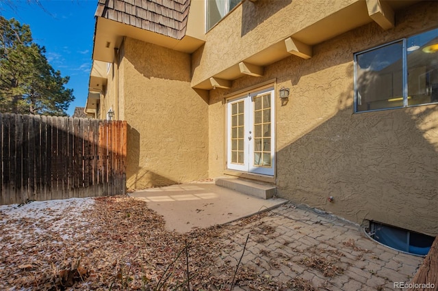 view of home's exterior featuring french doors, stucco siding, mansard roof, a patio area, and fence