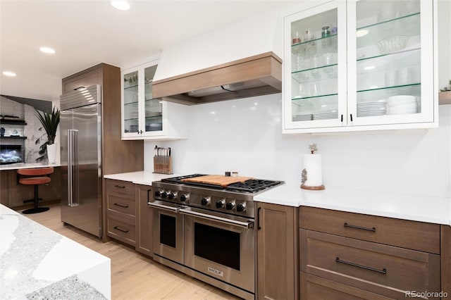 1 Club Ln, Littleton, CO 80123 - kitchen with premium appliances, light wood-style flooring, glass insert cabinets, recessed lighting, and premium range hood