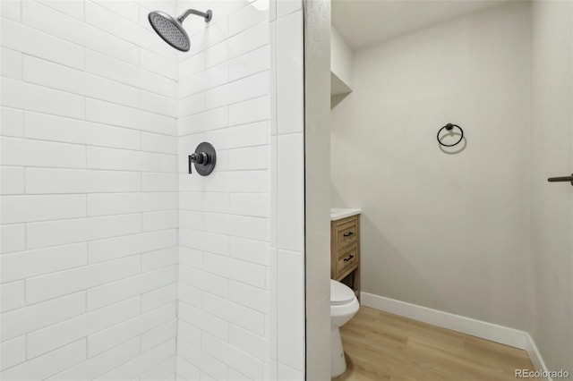 bathroom featuring a tile shower, hardwood / wood-style floors, vanity, and toilet