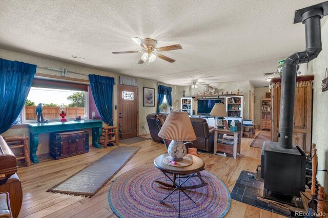 living room with a textured ceiling, ceiling fan, hardwood / wood-style floors, and a wood stove