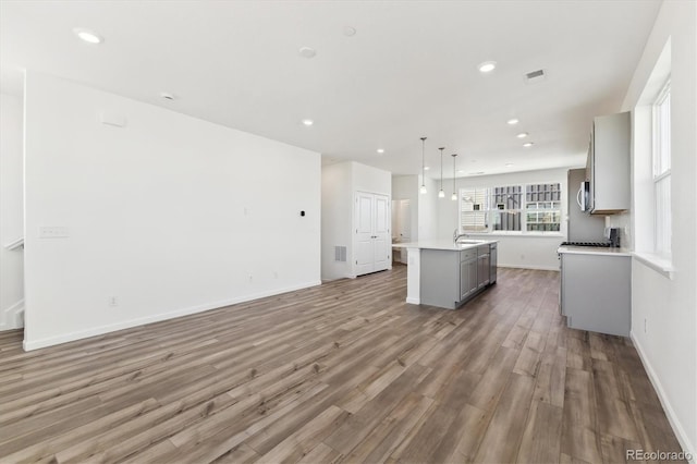 kitchen featuring a sink, wood finished floors, open floor plan, gray cabinets, and a center island with sink