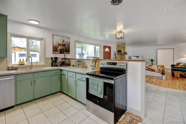 kitchen with stainless steel appliances, green cabinets, a sink, a peninsula, and tasteful backsplash