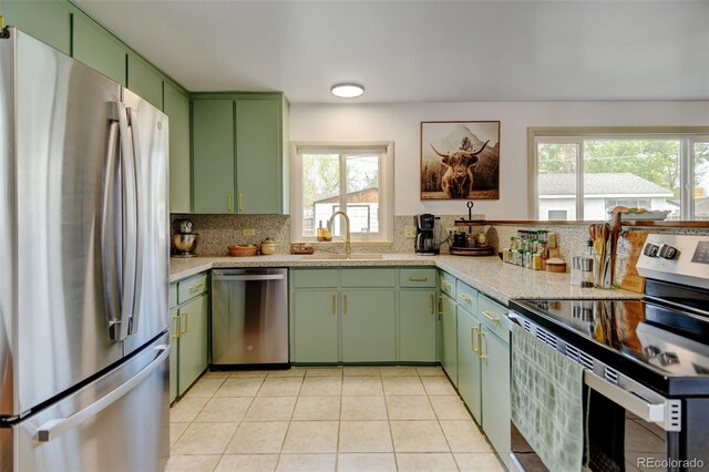 kitchen with stainless steel appliances, green cabinets, a sink, and light countertops
