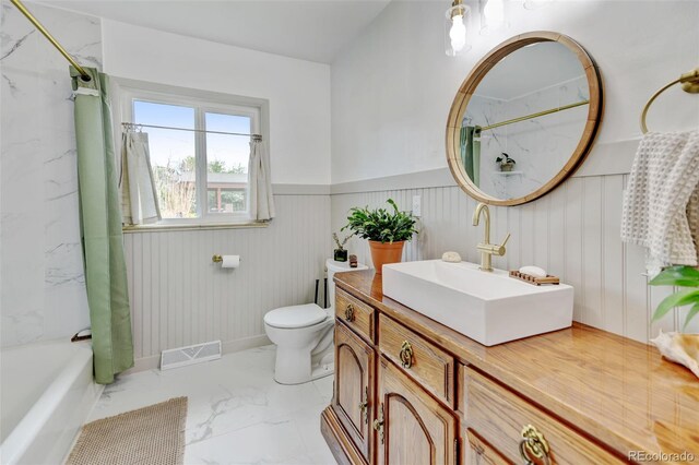 bathroom with marble finish floors, toilet, vanity, wainscoting, and shower / bath combination with curtain