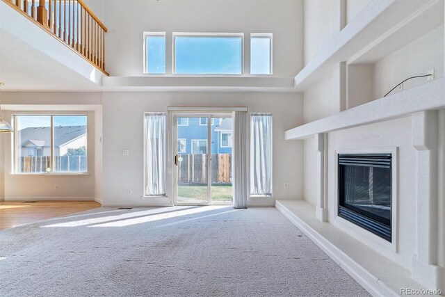 unfurnished living room with plenty of natural light, a high ceiling, and light colored carpet