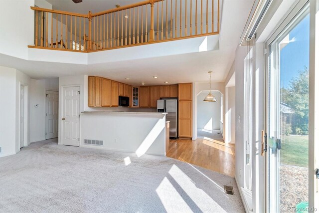 interior space with hanging light fixtures, a high ceiling, stainless steel fridge, and light hardwood / wood-style floors