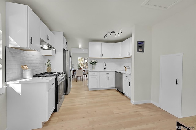 kitchen with appliances with stainless steel finishes, sink, white cabinetry, and light hardwood / wood-style floors