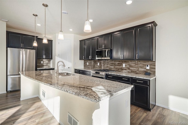 kitchen featuring appliances with stainless steel finishes, tasteful backsplash, a kitchen island with sink, sink, and decorative light fixtures