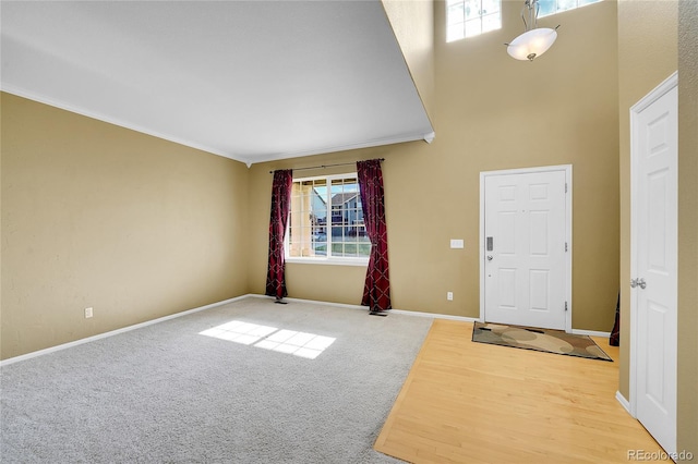 entryway with ornamental molding, baseboards, a towering ceiling, and carpet flooring