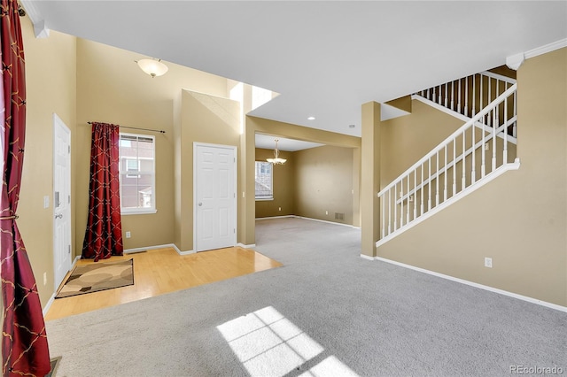 unfurnished living room with carpet, baseboards, stairway, wood finished floors, and a chandelier