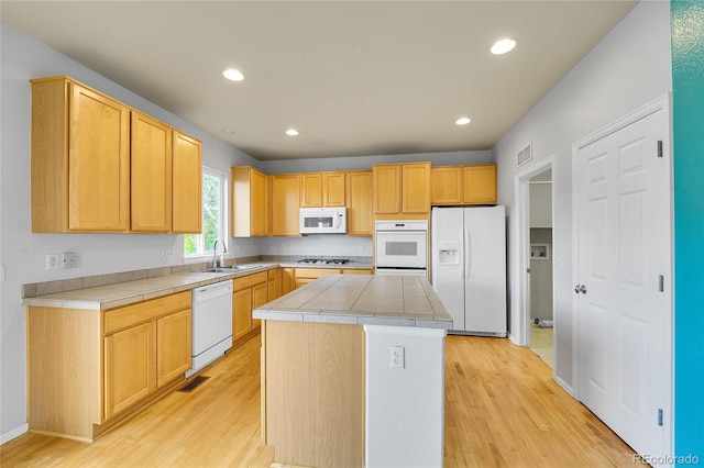 kitchen with white appliances, a sink, light wood finished floors, light brown cabinets, and a center island