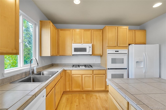 kitchen with white appliances, tile countertops, a sink, light wood finished floors, and light brown cabinets