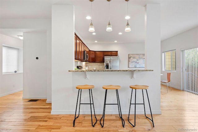 4190 W Alameda Ave, Denver, CO 80219 - kitchen with stainless steel fridge with ice dispenser, a breakfast bar area, light wood-style flooring, light stone counters, and backsplash