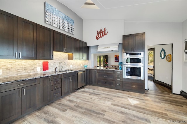 5607 Crawford Gulch Rd, Golden, CO 80403 - kitchen featuring appliances with stainless steel finishes, dark brown cabinets, light wood-style floors, light stone counters, and decorative backsplash