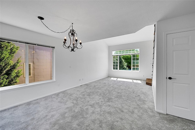 carpeted empty room featuring a chandelier and baseboards