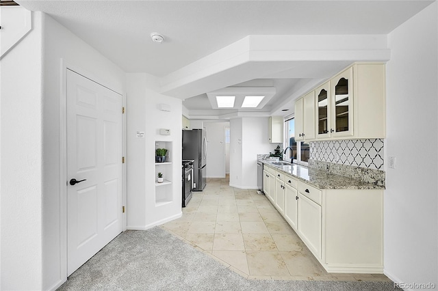 kitchen with a sink, glass insert cabinets, stainless steel appliances, light stone countertops, and tasteful backsplash