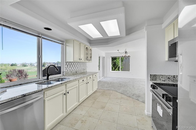 kitchen featuring stainless steel appliances, light colored carpet, a sink, light stone countertops, and a chandelier