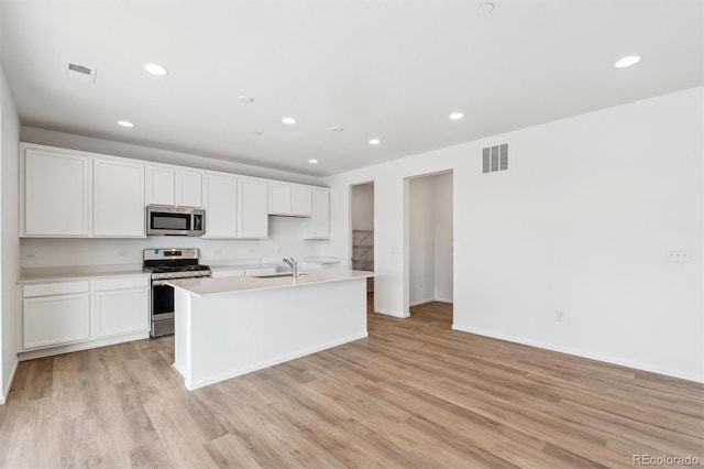 kitchen featuring sink, a center island with sink, light wood-type flooring, appliances with stainless steel finishes, and white cabinets