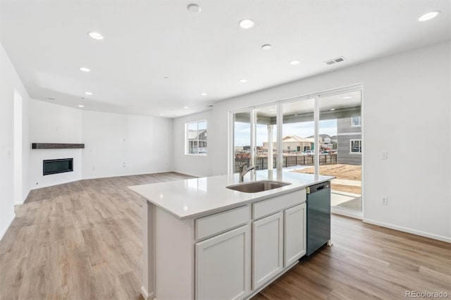 kitchen featuring white cabinetry, sink, a kitchen island with sink, stainless steel dishwasher, and light wood-type flooring