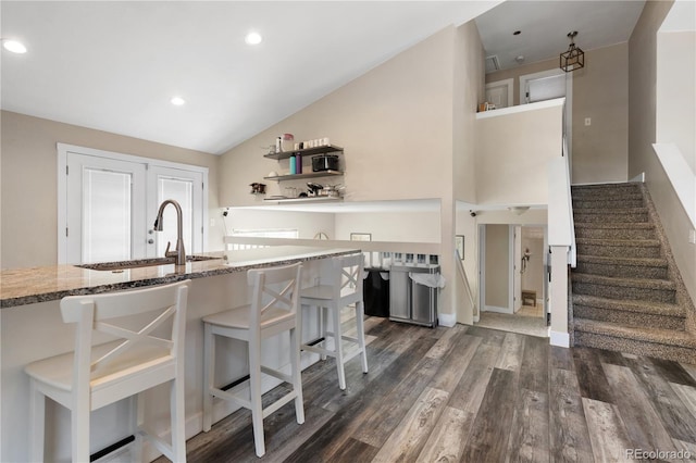 kitchen featuring stone counters, sink, a kitchen bar, vaulted ceiling, and dark wood-type flooring