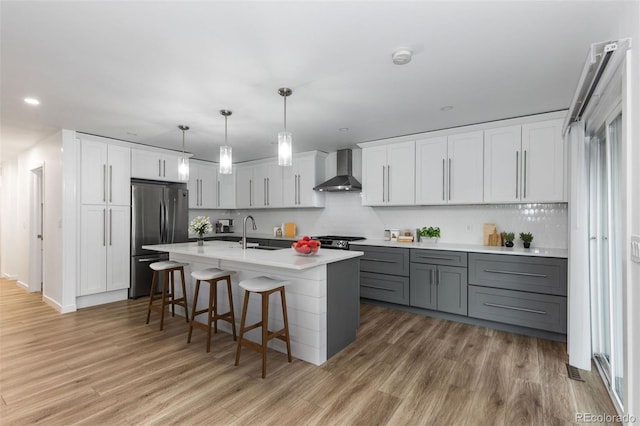 kitchen with freestanding refrigerator, wall chimney exhaust hood, a sink, light wood-style floors, and recessed lighting