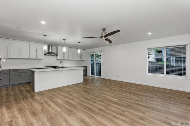 kitchen with wall chimney exhaust hood, light countertops, baseboards, a ceiling fan, and backsplash