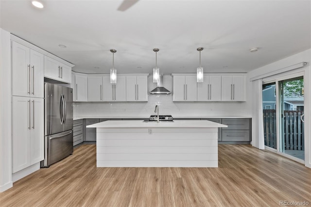 kitchen with stainless steel fridge, wall chimney range hood, light countertops, light wood-style flooring, and recessed lighting