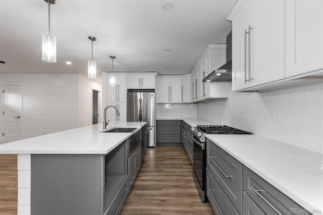 kitchen featuring appliances with stainless steel finishes, gray cabinets, wall chimney range hood, a sink, and dark wood-style flooring