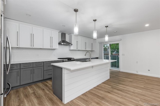 kitchen featuring wall chimney range hood, a sink, decorative backsplash, stainless steel appliances, and light wood-type flooring