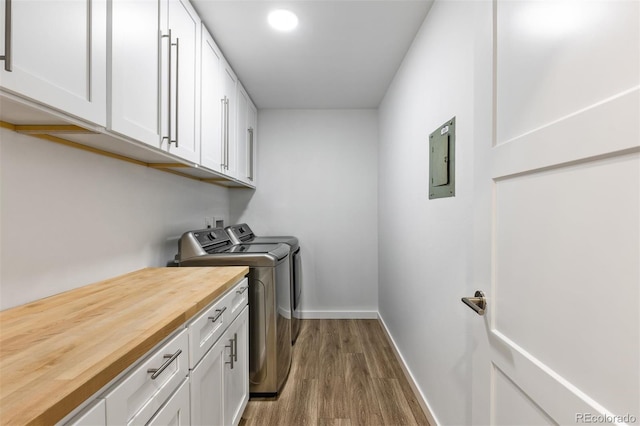 washroom with washing machine and dryer, cabinet space, wood finished floors, baseboards, and electric panel