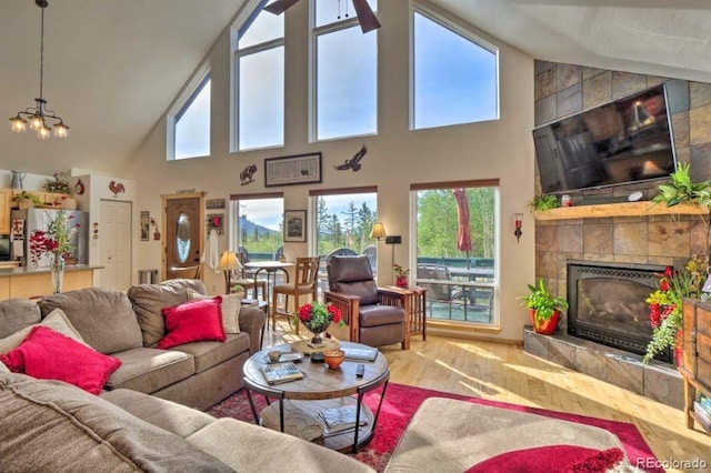 living room featuring a tiled fireplace, hardwood / wood-style floors, high vaulted ceiling, and a chandelier