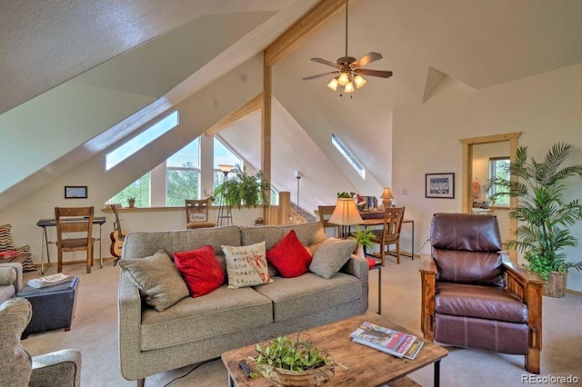 carpeted living room with a skylight, ceiling fan, beamed ceiling, and high vaulted ceiling