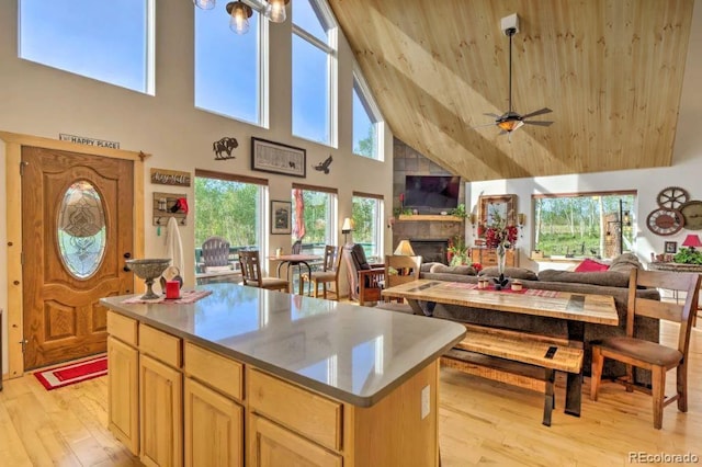 kitchen with light brown cabinetry, high vaulted ceiling, a fireplace, a center island, and light hardwood / wood-style floors