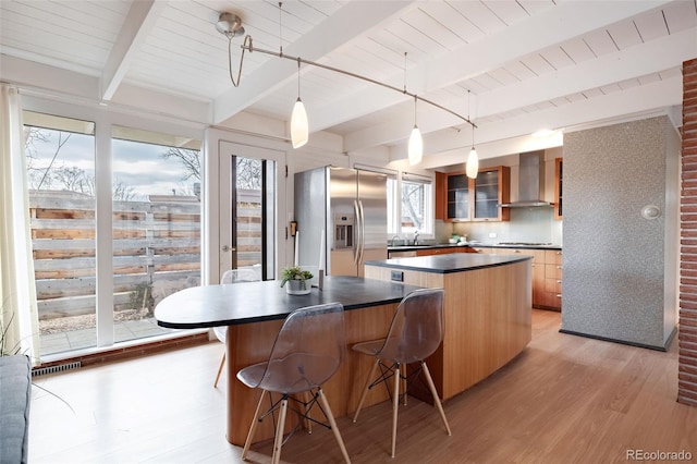 kitchen with pendant lighting, wall chimney range hood, a center island, stainless steel refrigerator with ice dispenser, and cooktop