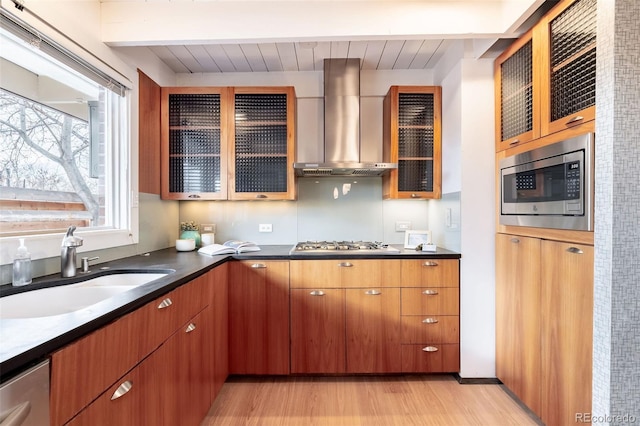 kitchen with appliances with stainless steel finishes, sink, light hardwood / wood-style floors, wall chimney range hood, and beam ceiling