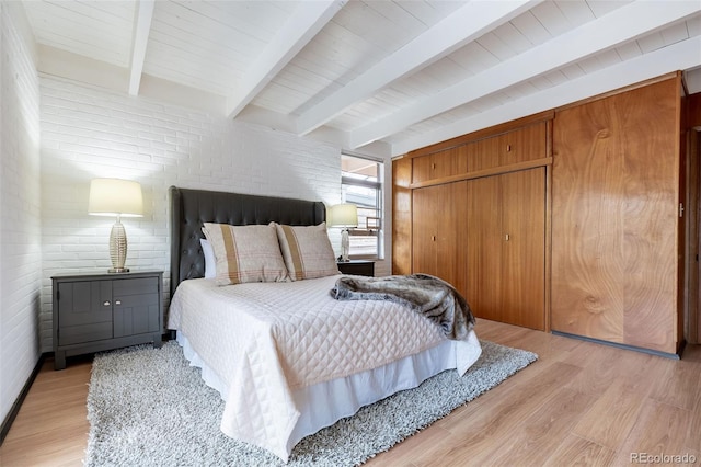 bedroom featuring beamed ceiling, brick wall, light hardwood / wood-style floors, and a closet