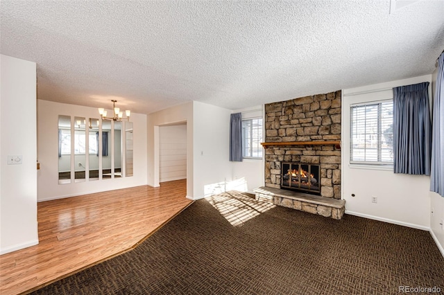 unfurnished living room with a textured ceiling, wood-type flooring, a chandelier, and a stone fireplace