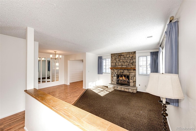 unfurnished living room with a textured ceiling, a notable chandelier, a fireplace, and wood-type flooring