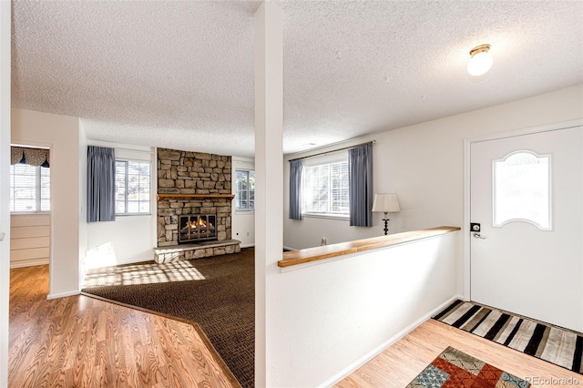 foyer entrance with plenty of natural light, a textured ceiling, wood-type flooring, and a stone fireplace