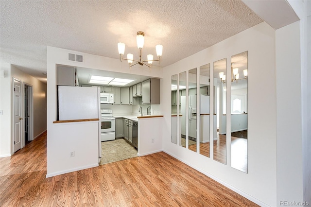 kitchen featuring white appliances, a chandelier, light hardwood / wood-style floors, a textured ceiling, and sink