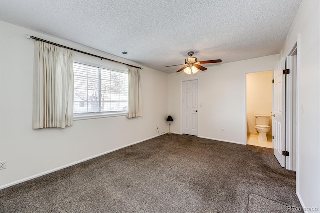 unfurnished bedroom with ensuite bathroom, a textured ceiling, dark colored carpet, and ceiling fan